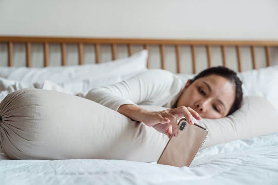 Woman leaning on her body pillow while looking at her phone