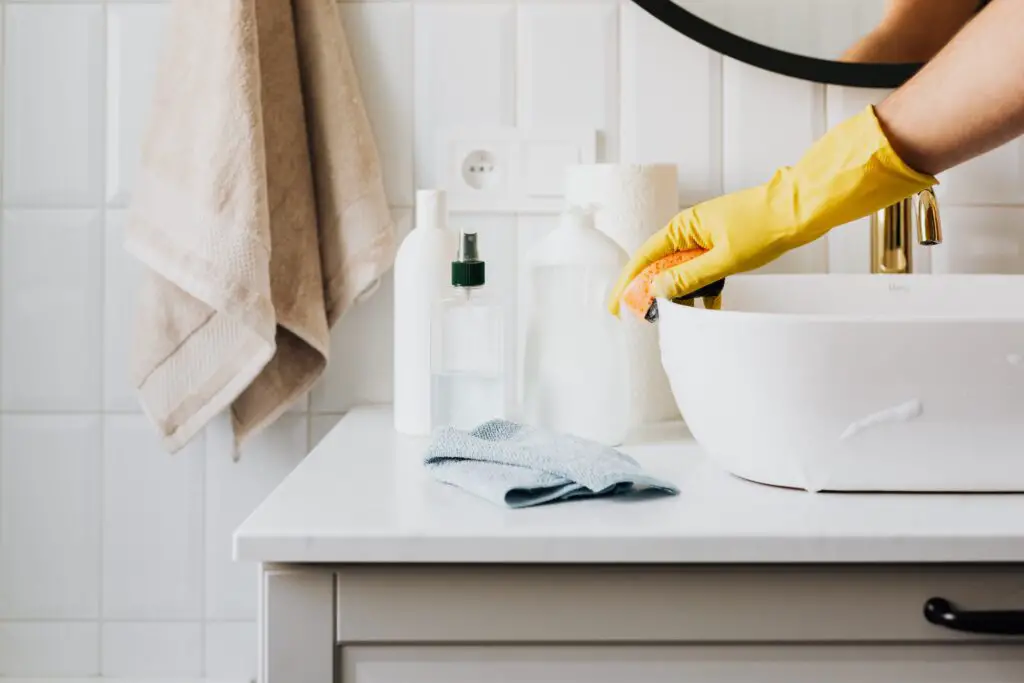 Un brazo con guantes amarillos limpiando el lavabo del baño.