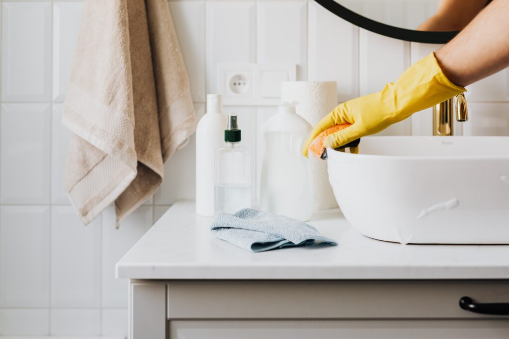 An arm with yellow gloves cleaning a bathroom sink