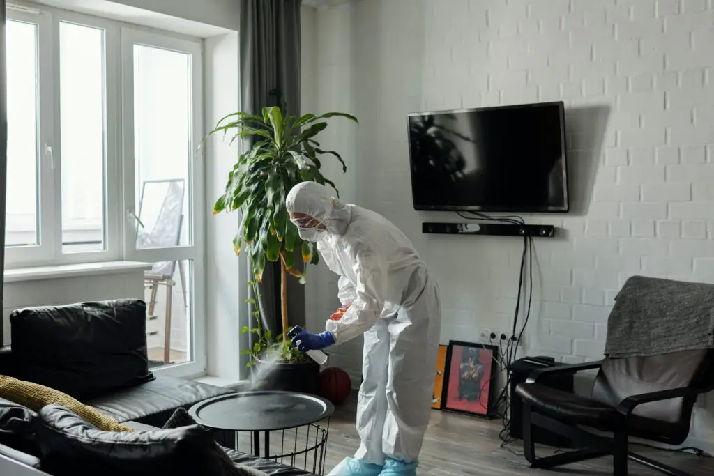 Una persona que usa un desinfectante y usa equipo de protección mientras limpia