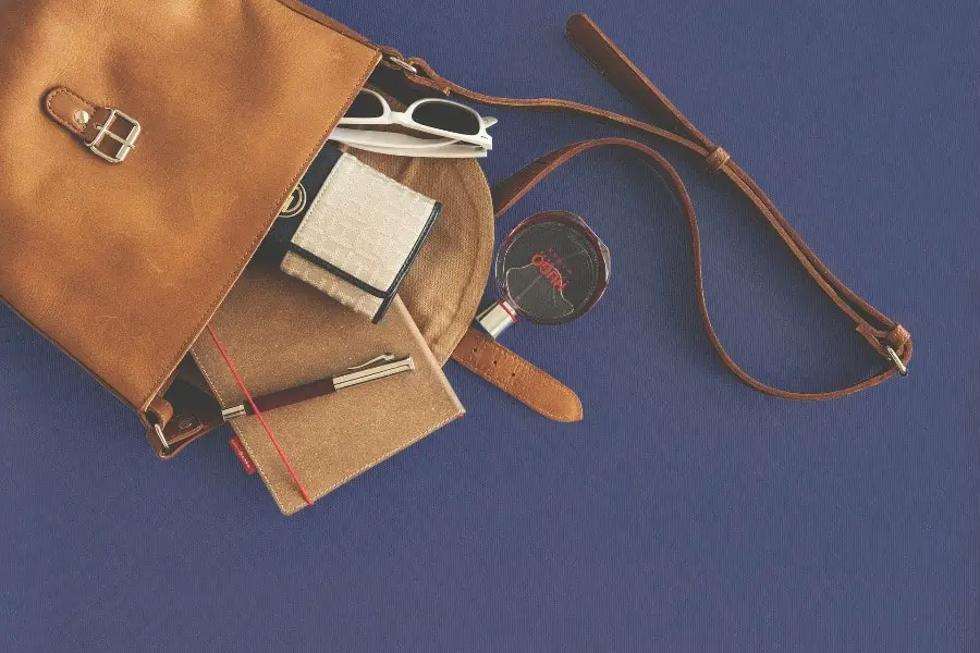 Perfume, notebook, wallet, ballpen and a sunglass are spilling out of a leather purse