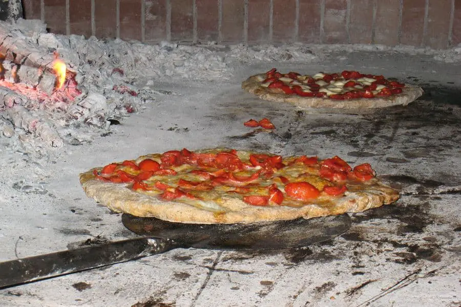 Two whole pizza being cooked in a brick oven
