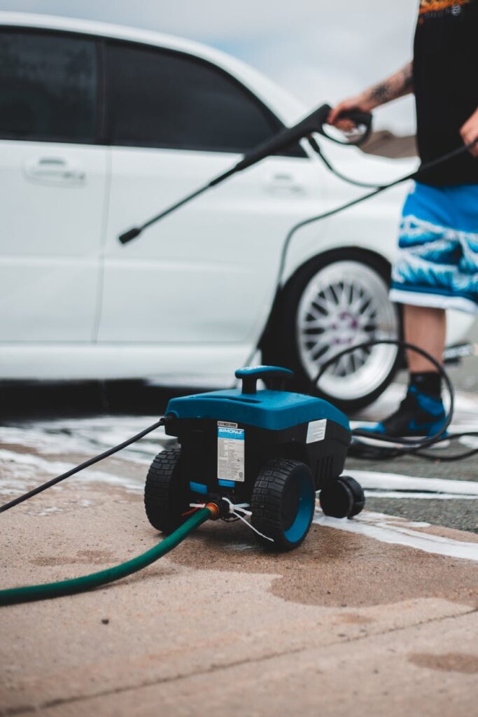 Man using a pressure washer to clean a car