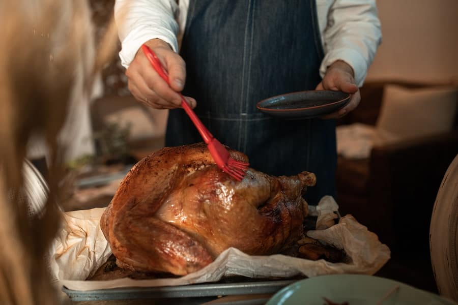 Person using a pastry brush on a roasted chicken