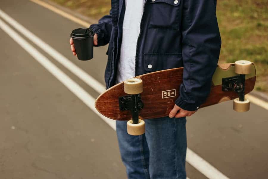 Man holding a skateboard and coffee