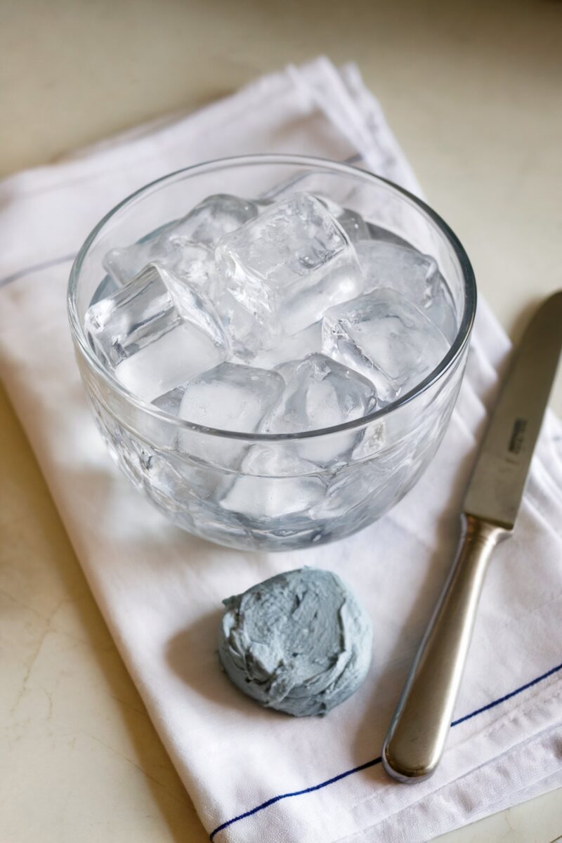 A bowl of ice cubes and a knife on a white cloth