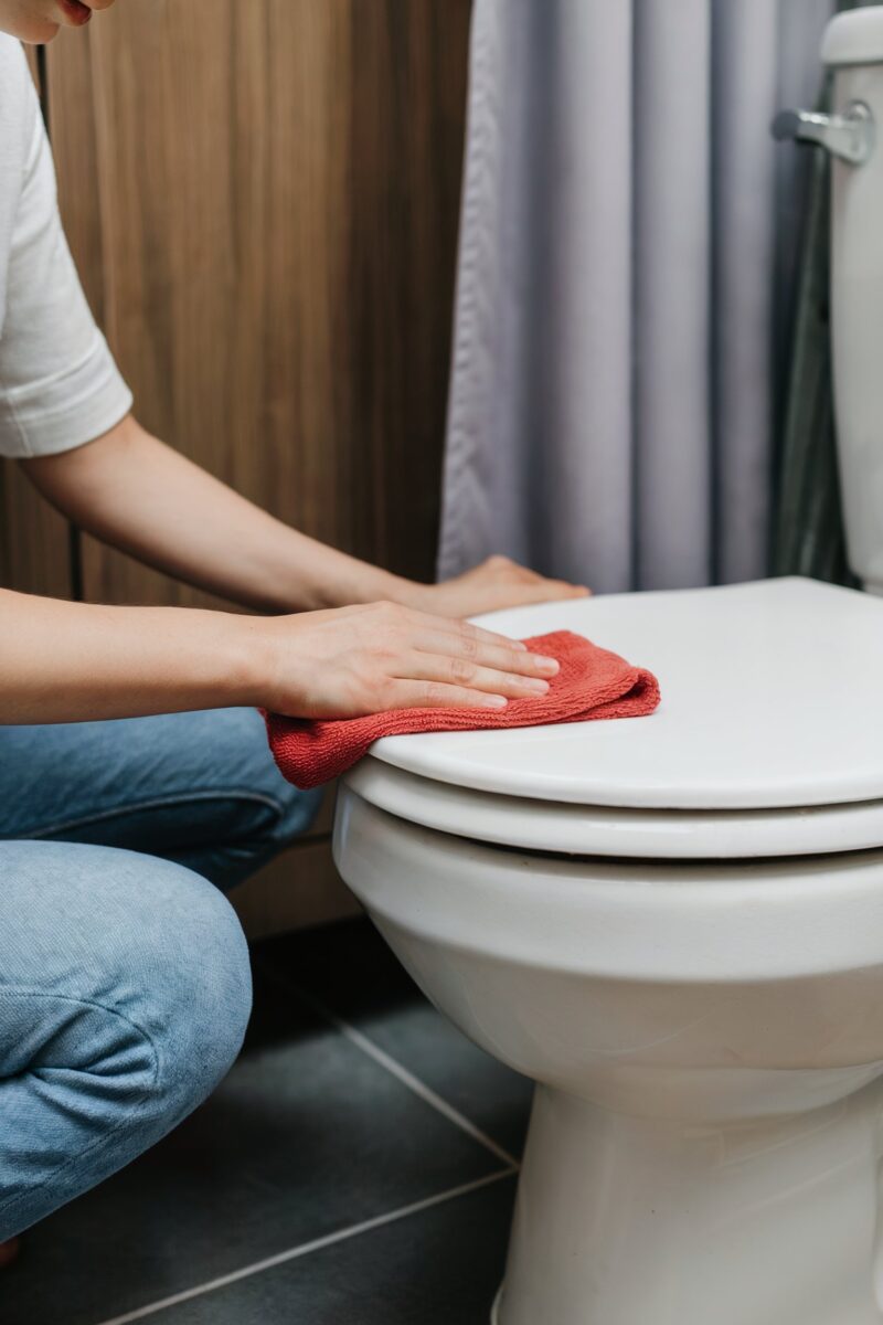 Person wiping down a toilet lid with a red cloth