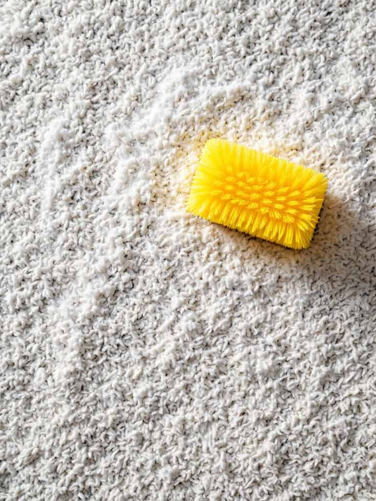 A yellow brush on a white carpet, indicating cleaning