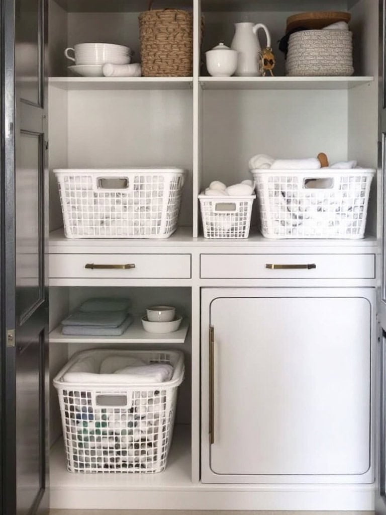 A neat laundry closet with labeled bins for sorting whites, colors, and delicates, and towels neatly stacked on a shelf.