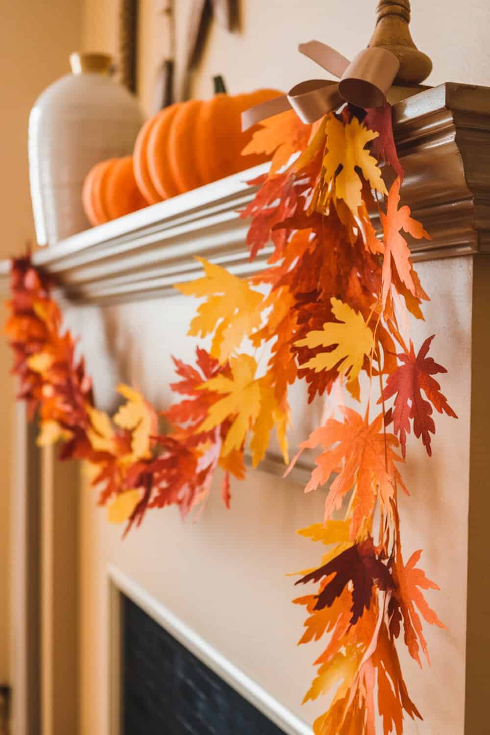 Colorful handmade leaf garland draped over a mantel with pumpkins in the background.