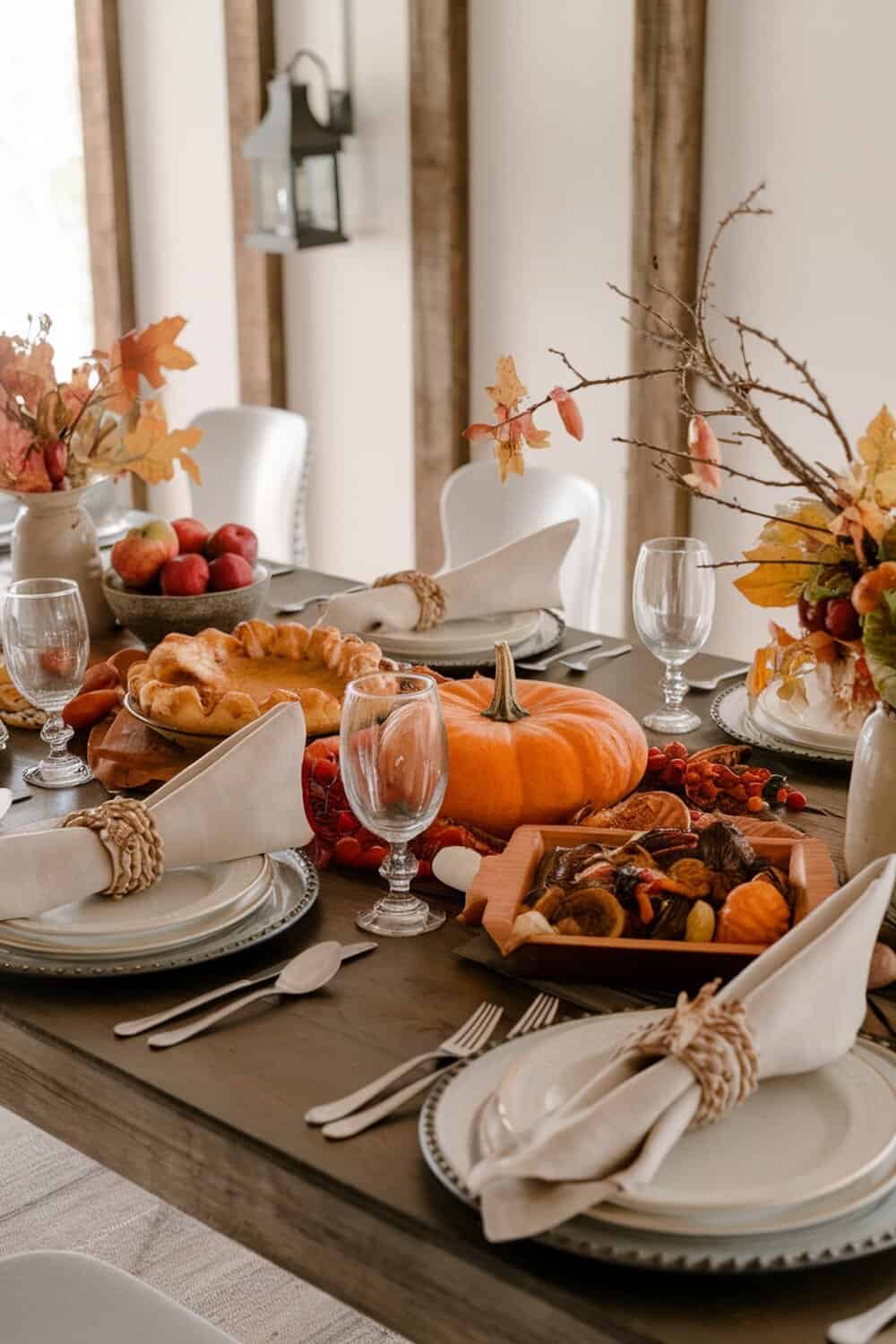 A beautifully arranged fall-themed table setting with pumpkins, apples, and autumn leaves.