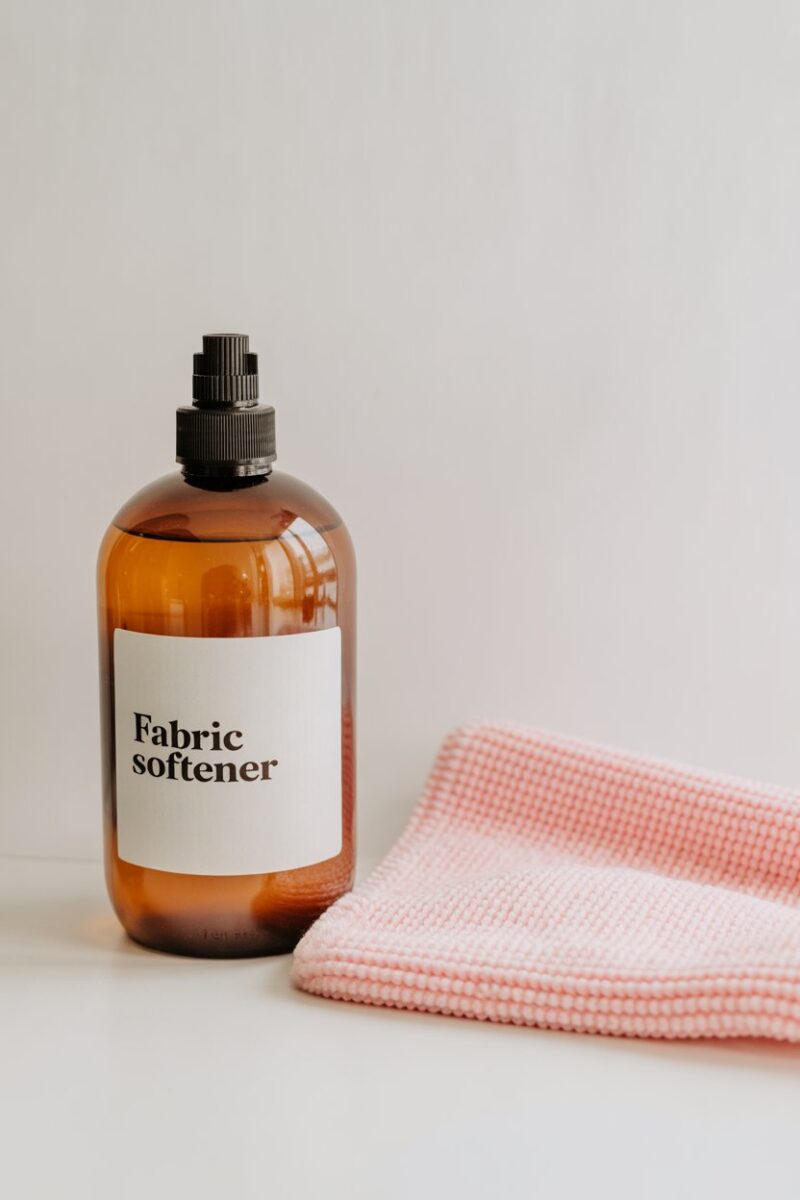 A bottle of fabric softener next to a pink microfiber cloth.