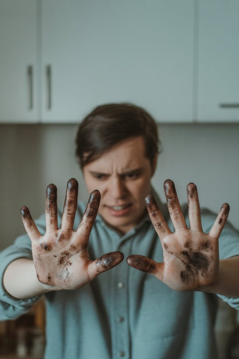 A person cleaning a surface with dirty hands, showing signs of frustration.