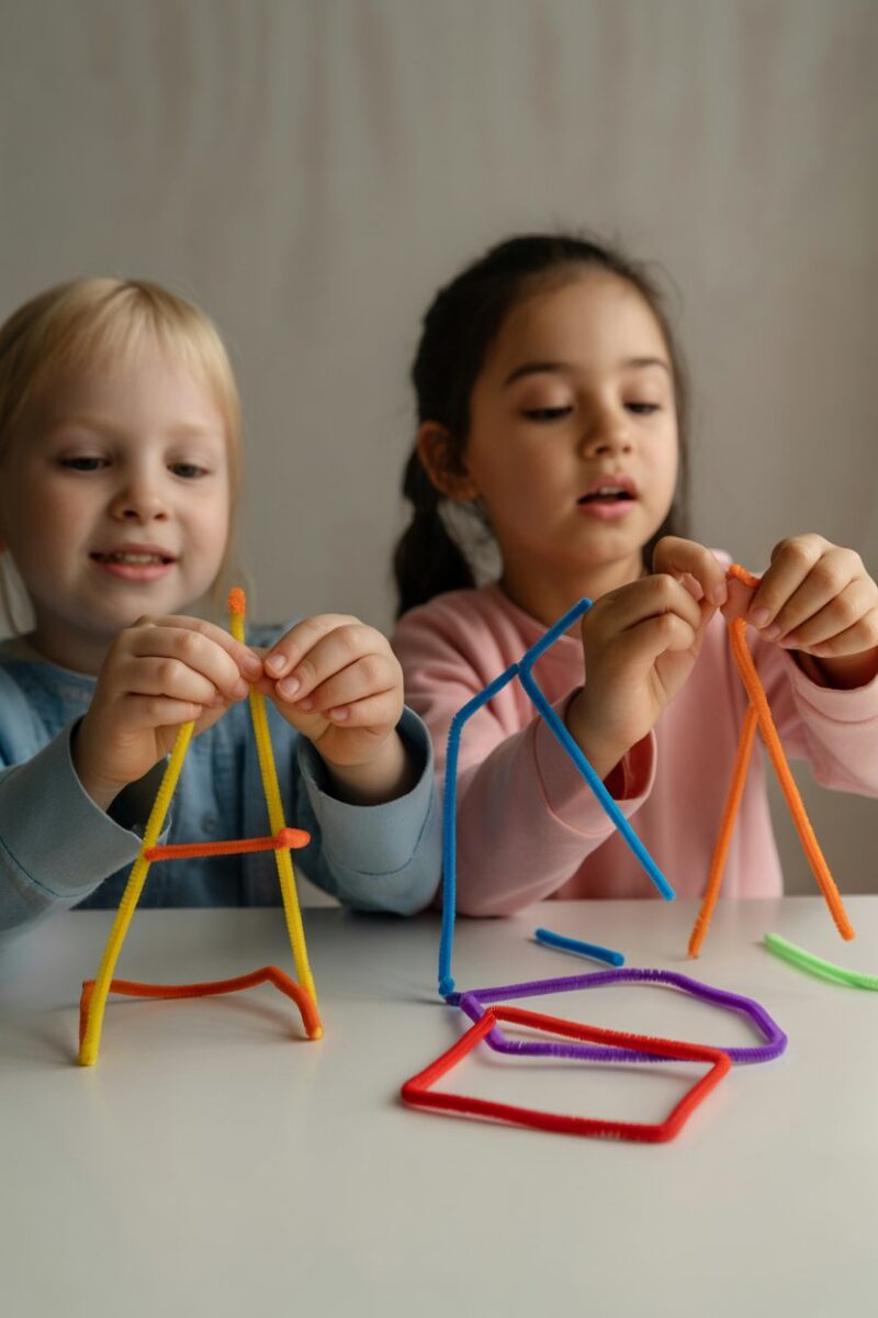 Children using colorful pipe cleaners to create shapes and structures at a table.