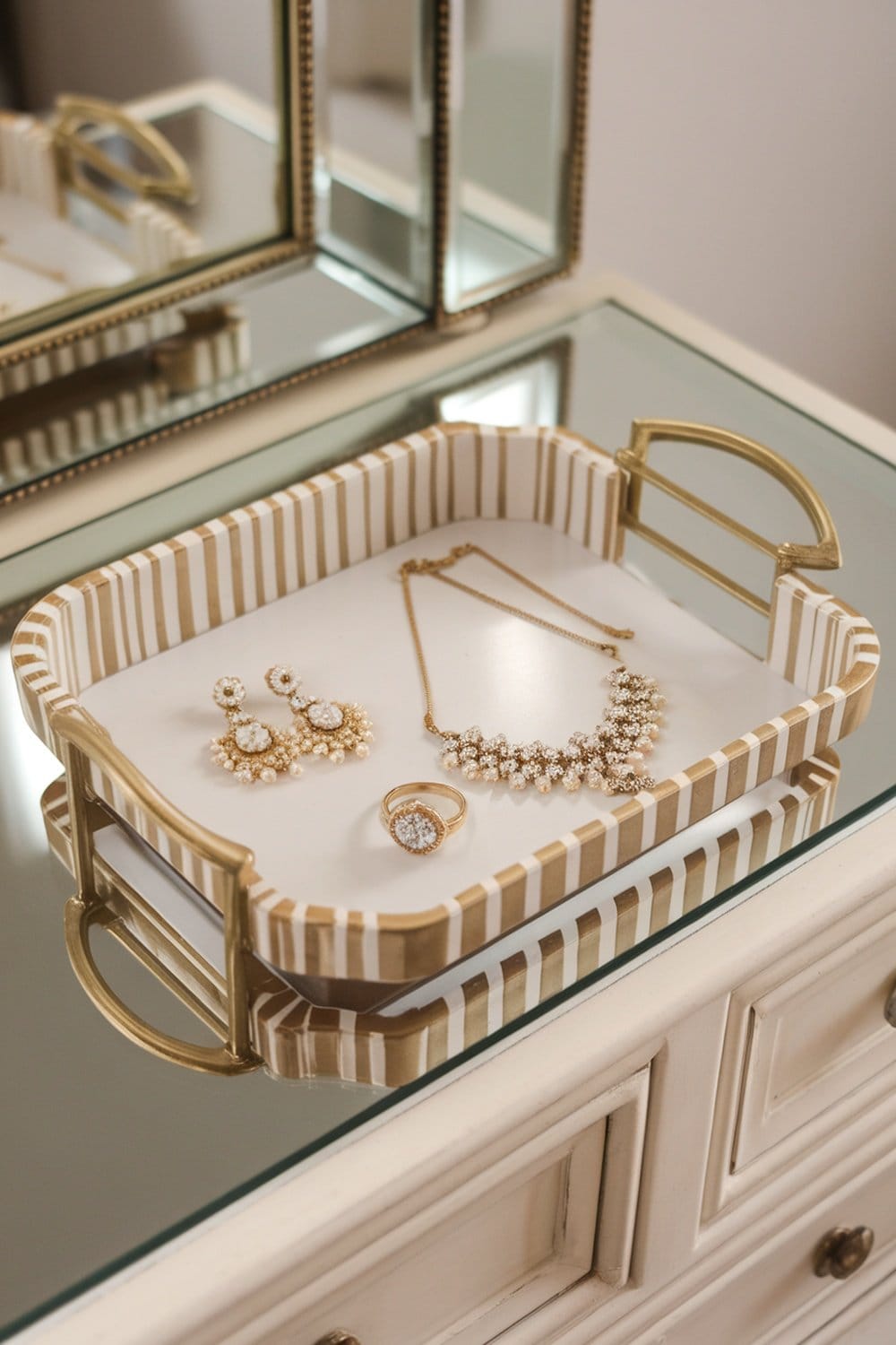 A decorative tray with jewelry including earrings, a necklace, and a ring, placed on a mirrored surface.