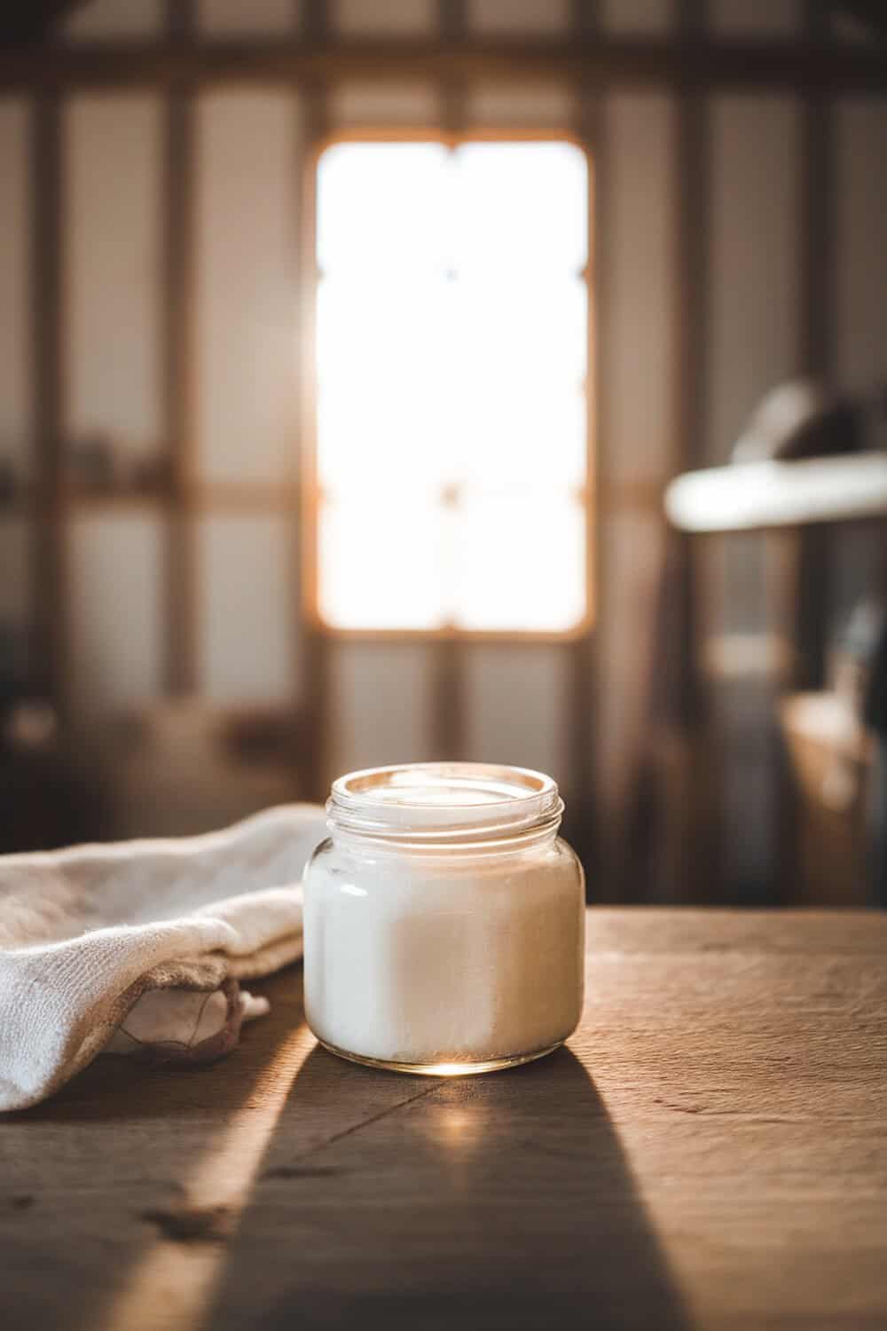 A jar of coconut oil on a wooden table with a cloth beside it.