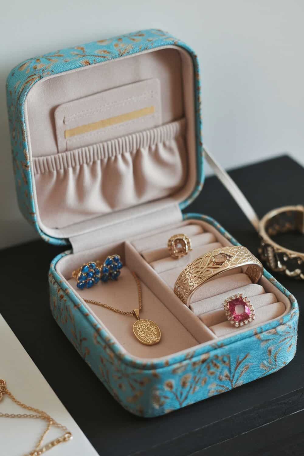 A fabric-covered jewelry box with various pieces of jewelry inside.
