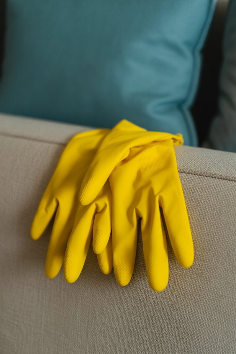 A pair of yellow rubber gloves resting on a light gray couch.