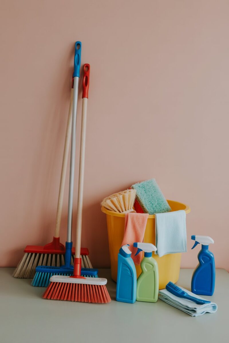 A variety of colorful cleaning tools including brooms, brushes, and cloths arranged on a table.