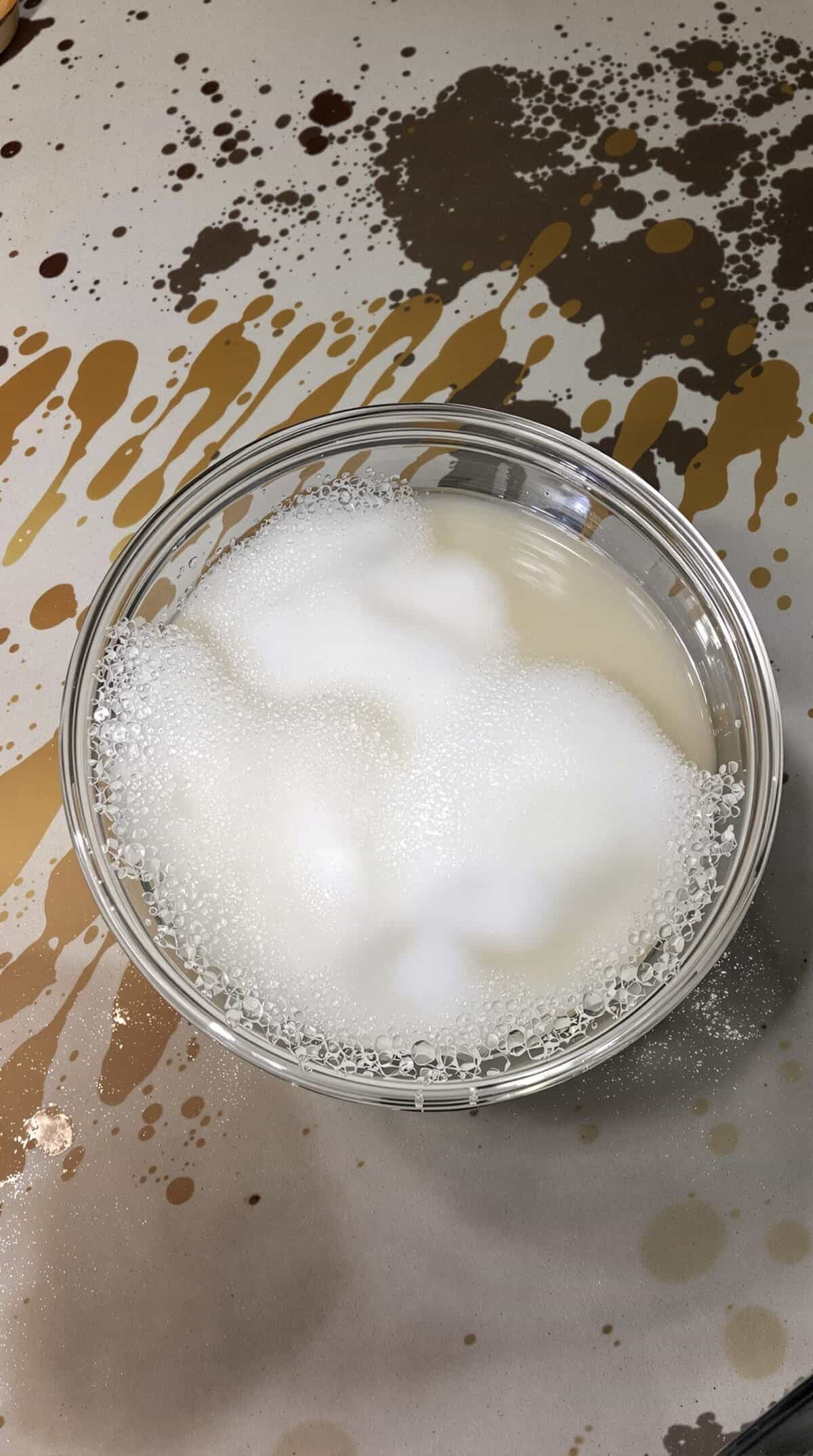 A bowl of bubbly vinegar and baking soda mixture on a stained surface.