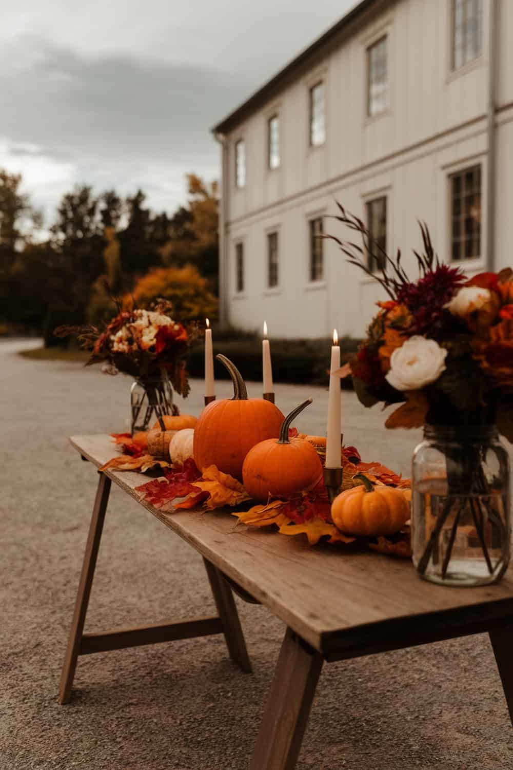 A rustic table setting featuring pumpkins, candles, and autumn leaves.