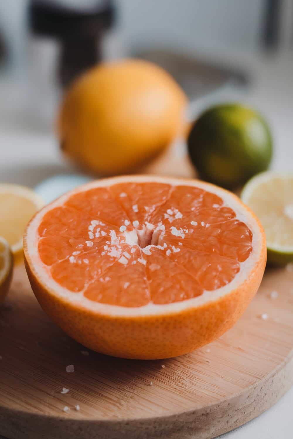 A halved grapefruit with salt on top, surrounded by whole citrus fruits.