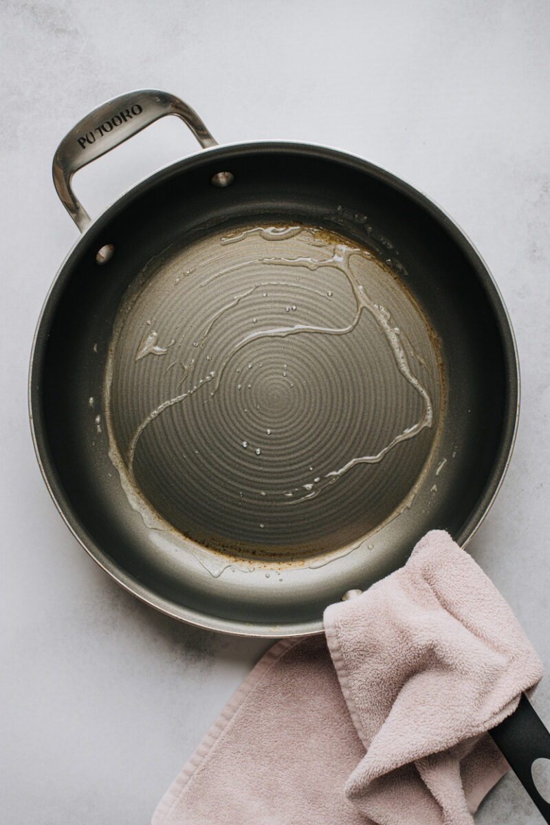 A frying pan with a little oil and a pink cloth on the handle.