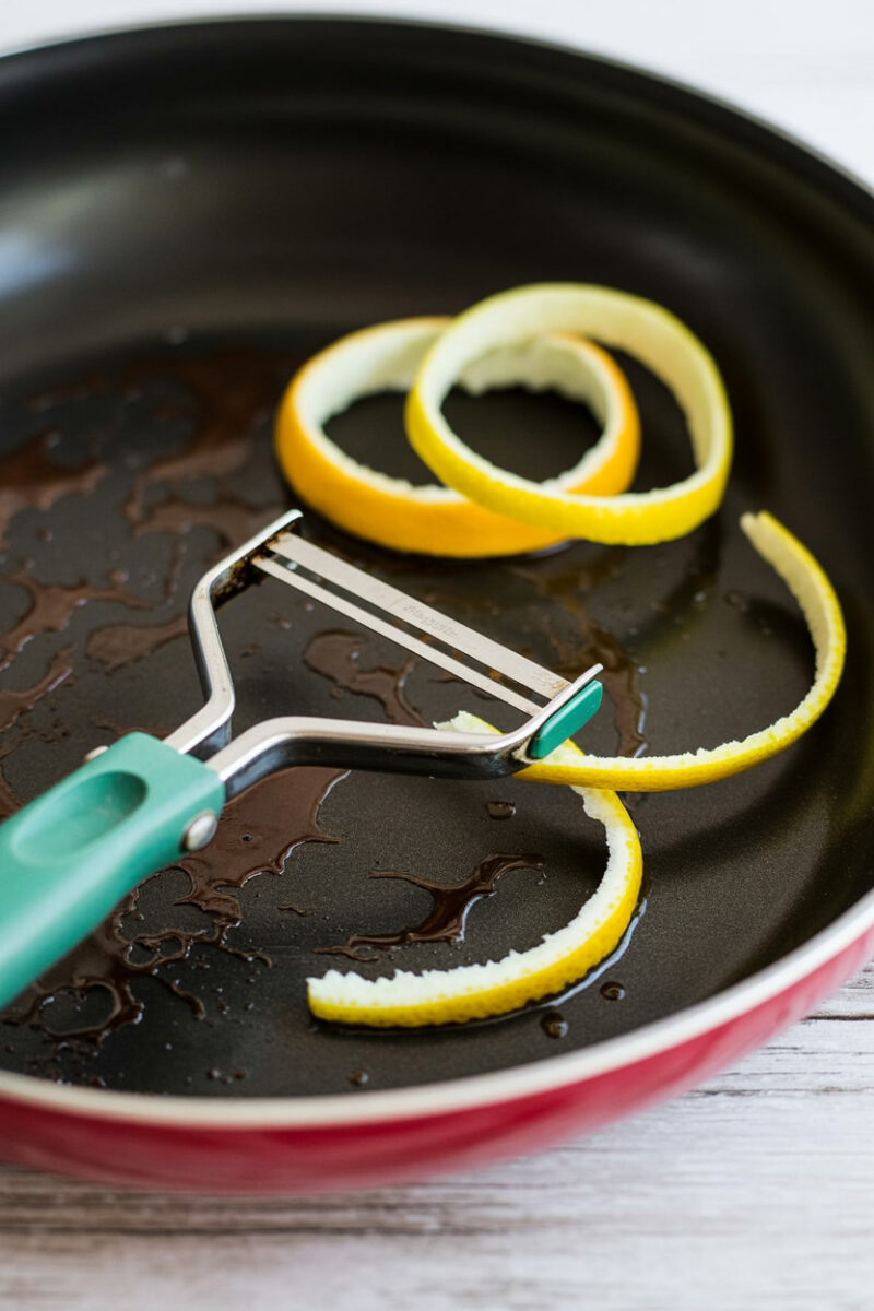 A pan with citrus peels and a peeler inside it.