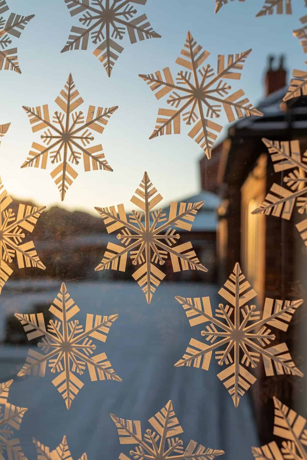 A window decorated with intricate paper snowflakes against a sunset backdrop.