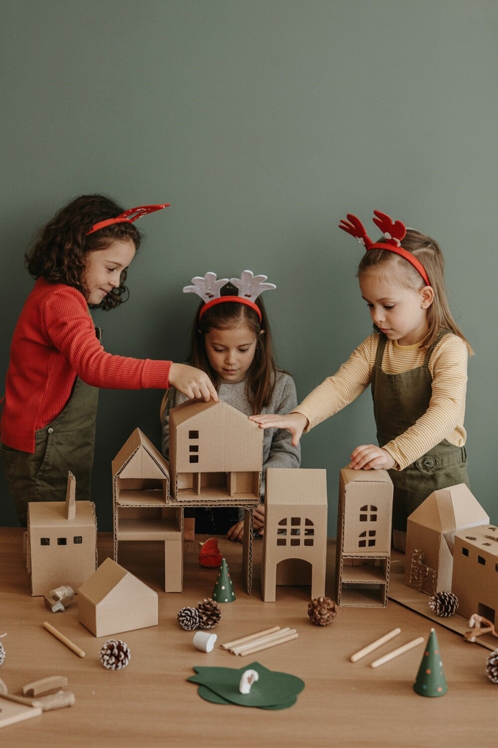 Kids building a cardboard Christmas village scene with decorations.