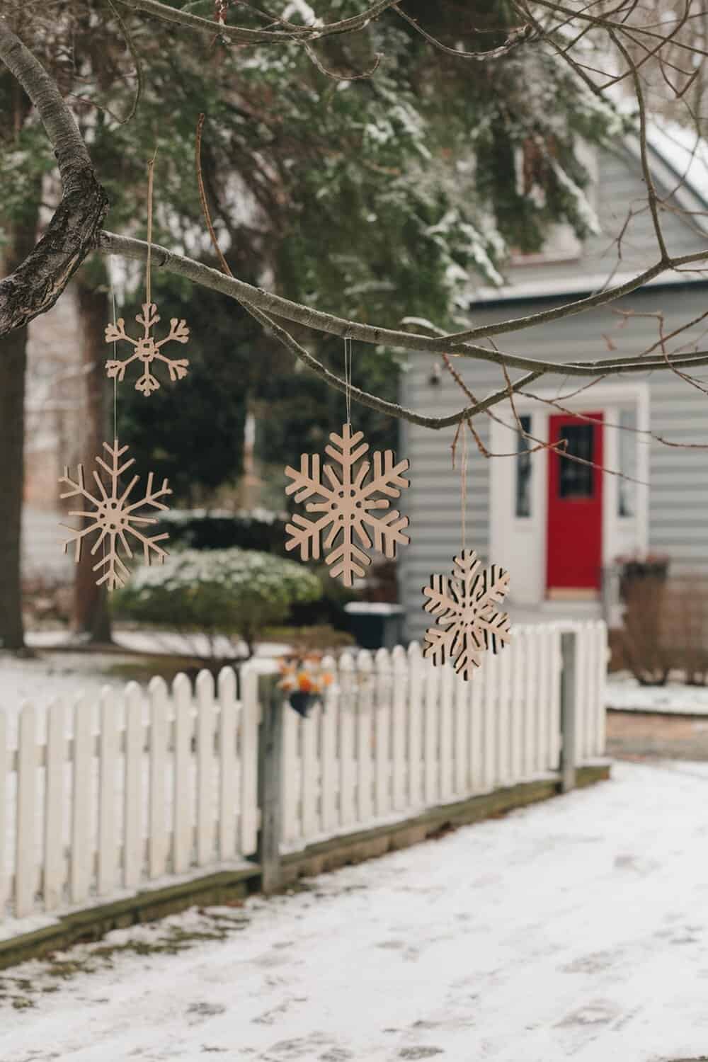 Rustic wooden snowflakes hanging from a tree branch in a snowy outdoor setting.