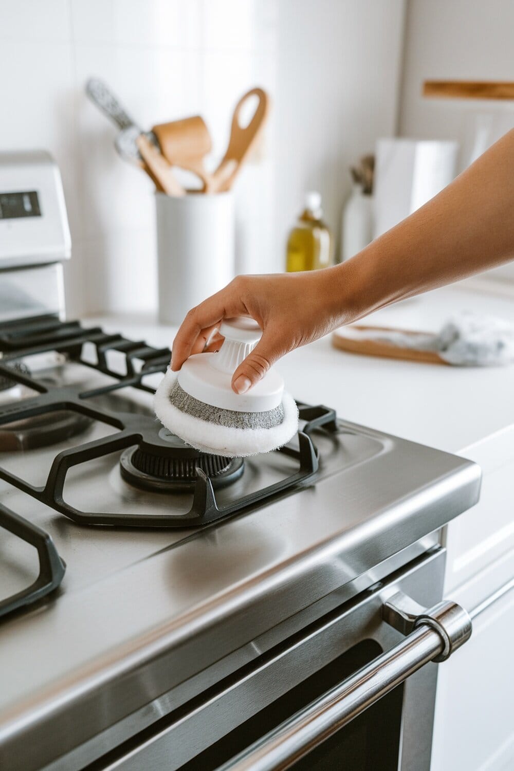 A person cleaning a stainless steel stove with a scrubber.