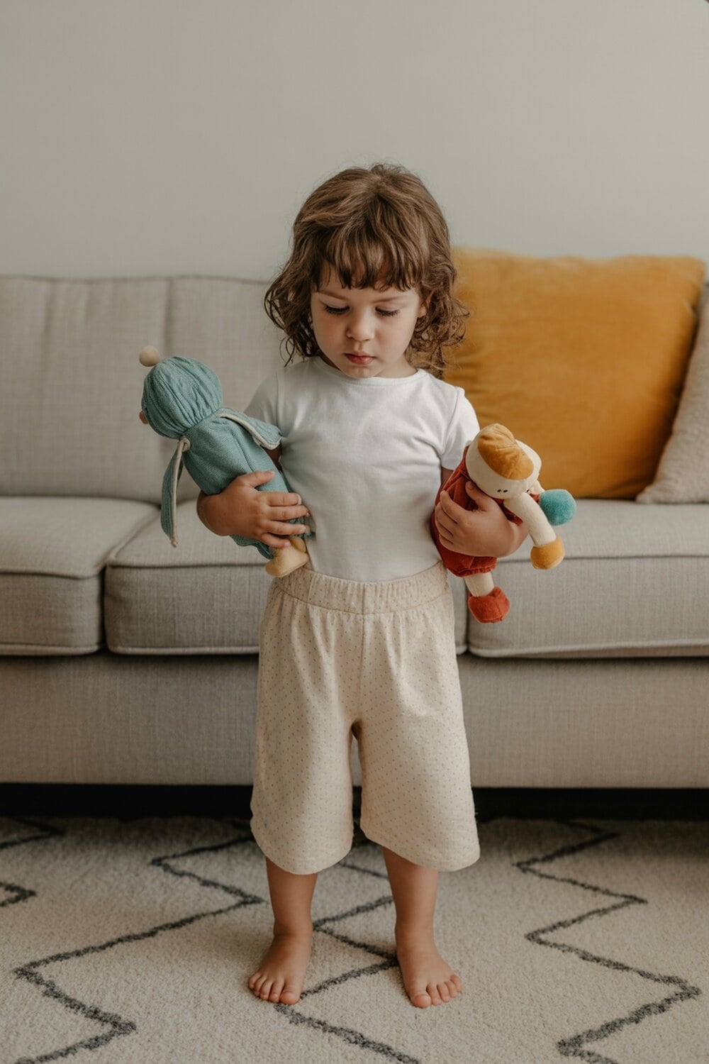 A child holding two stuffed toys, looking thoughtful.