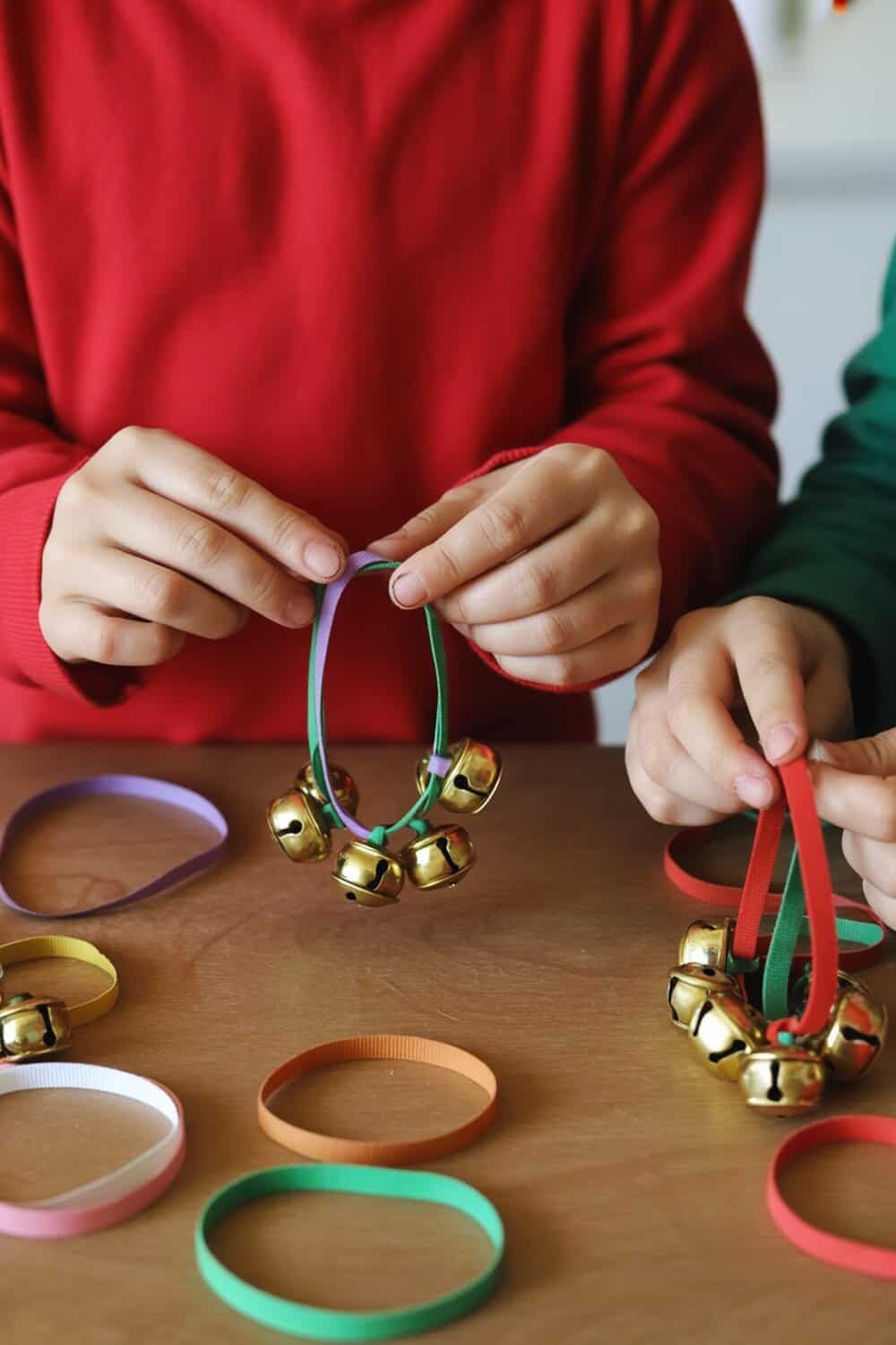 Children making jingle bell bracelets with colorful ribbons and bells.