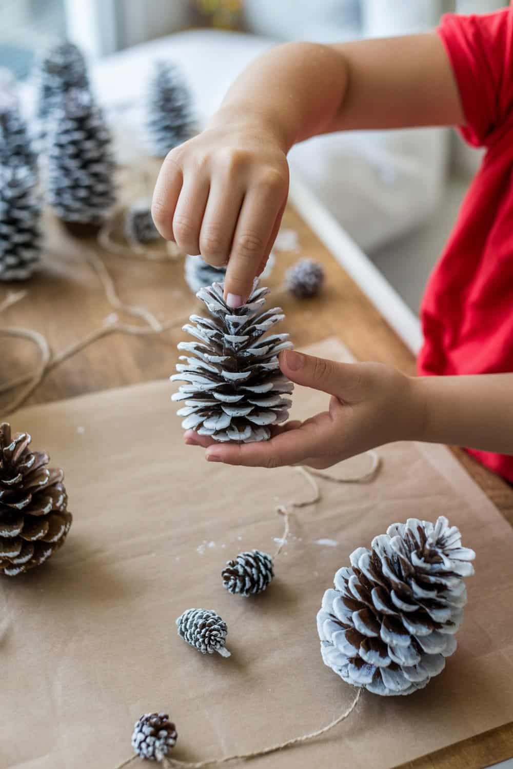 A child decorating pinecones with white glue and glitter for Christmas ornaments.