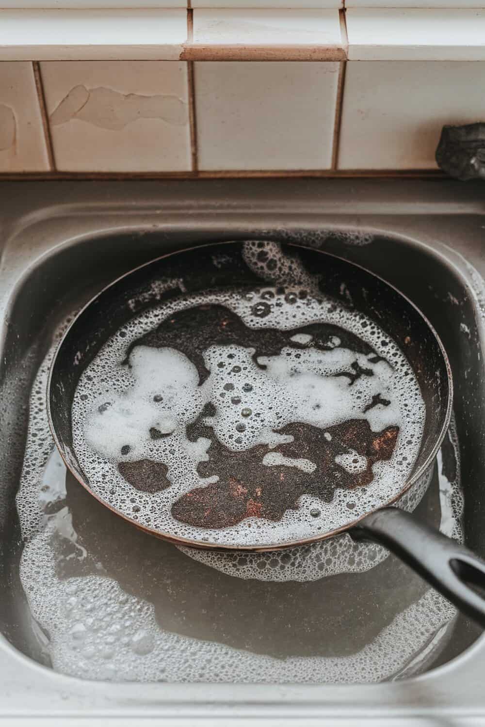 A burnt pan soaking in soapy water in a sink.