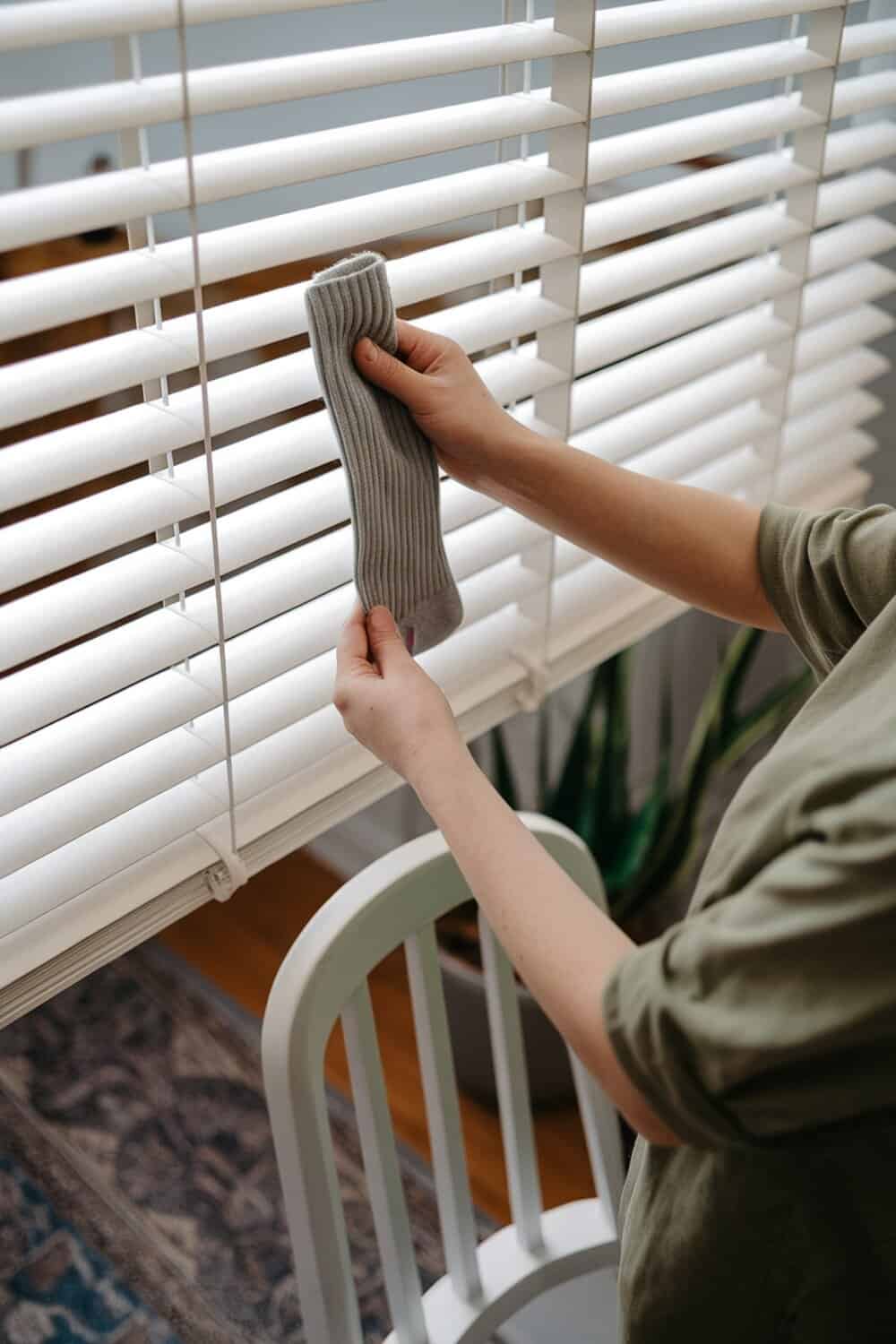A person dusting blinds with a sock