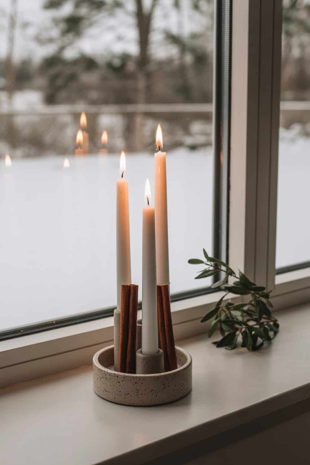 Cinnamon stick candle holders with white candles on a windowsill.