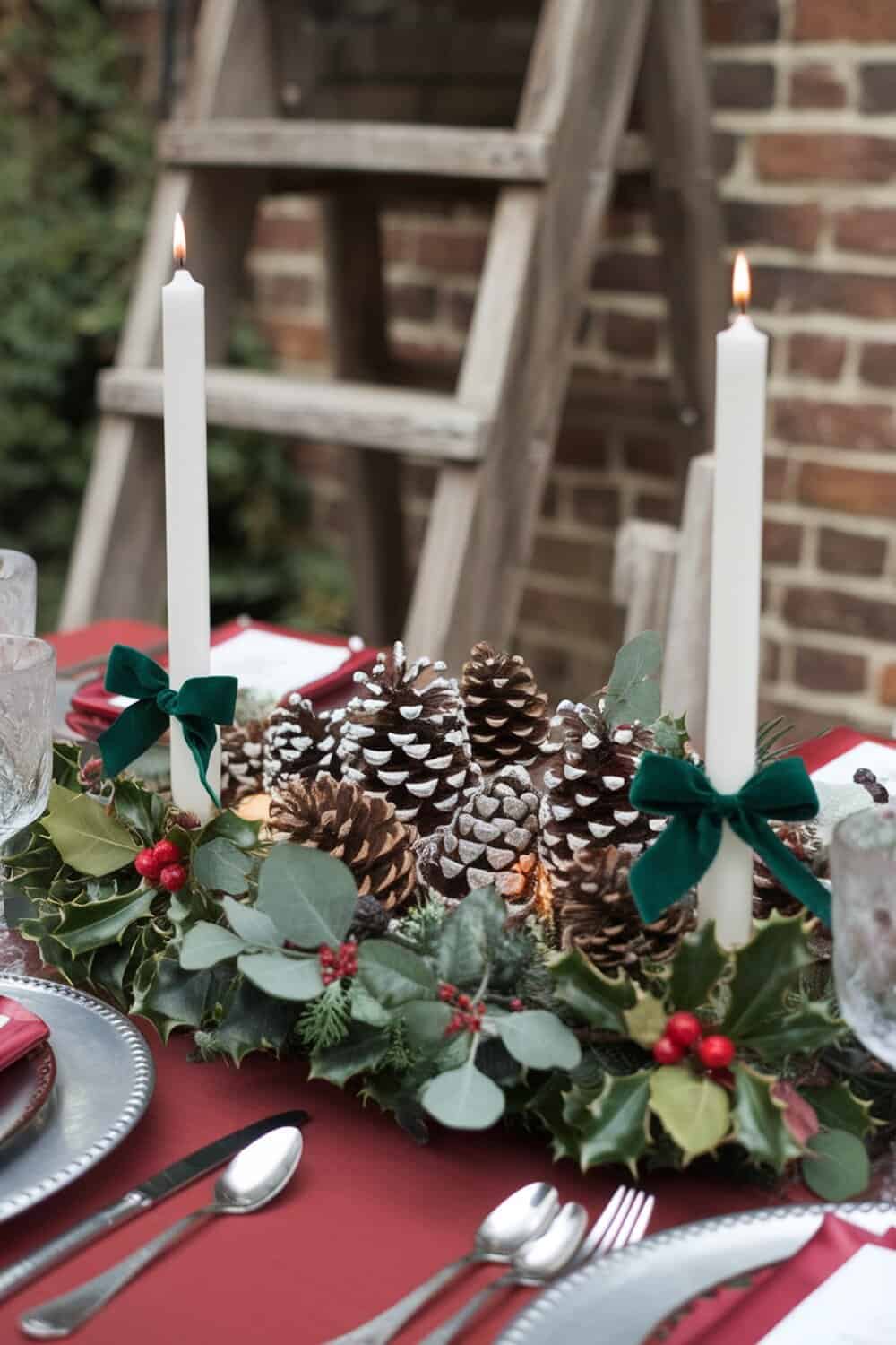 A holiday centerpiece featuring pinecones, greenery, and candles on a table.