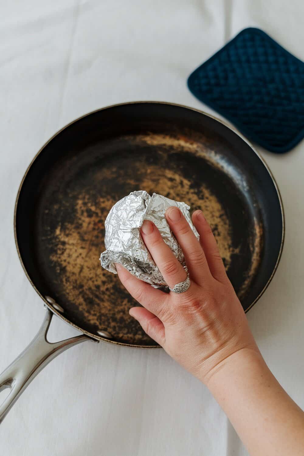 A hand using a crumpled aluminum foil ball to scrub a burnt pan.