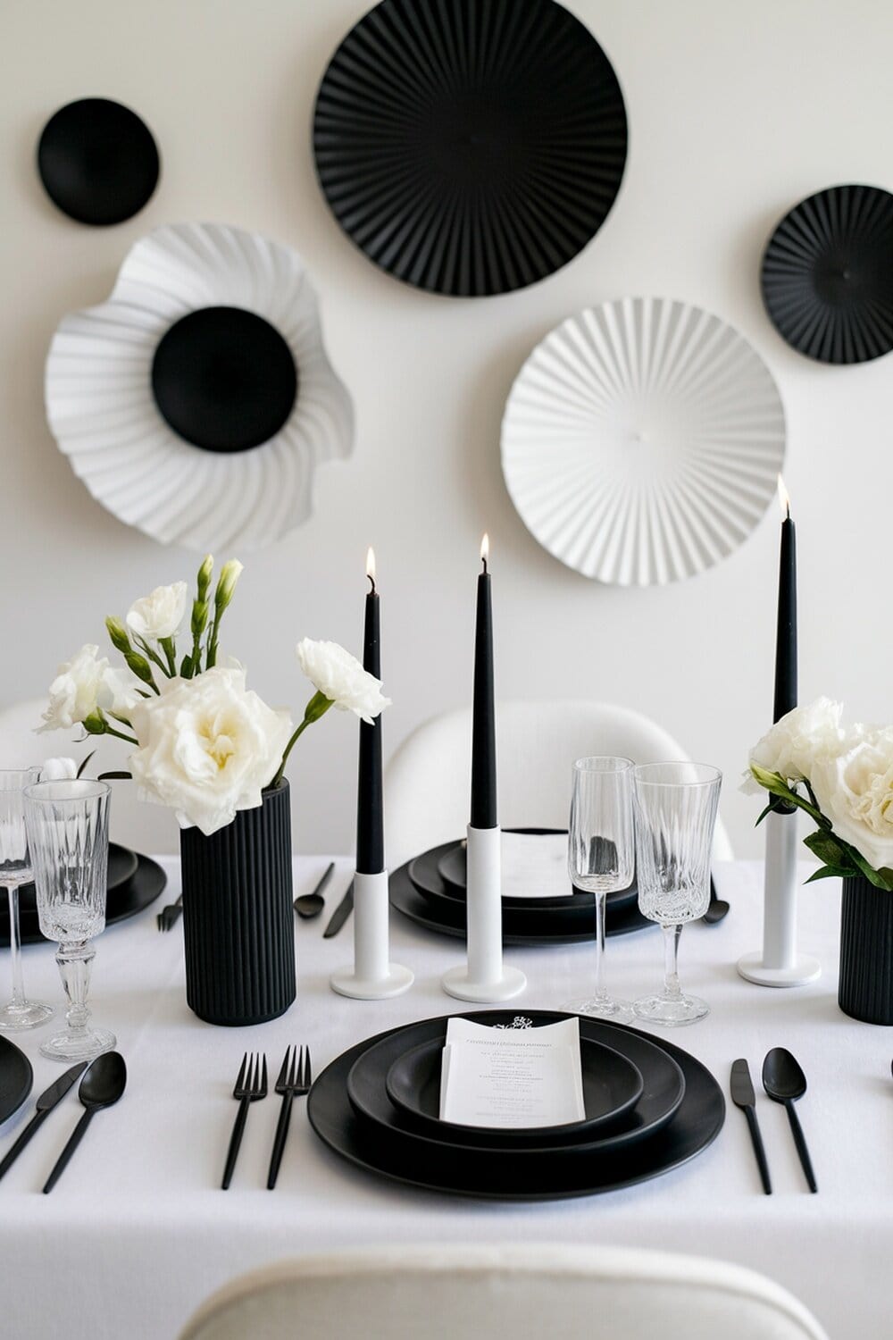 A beautifully set Christmas table with black and white decorations, featuring black plates, white flowers, and candles.