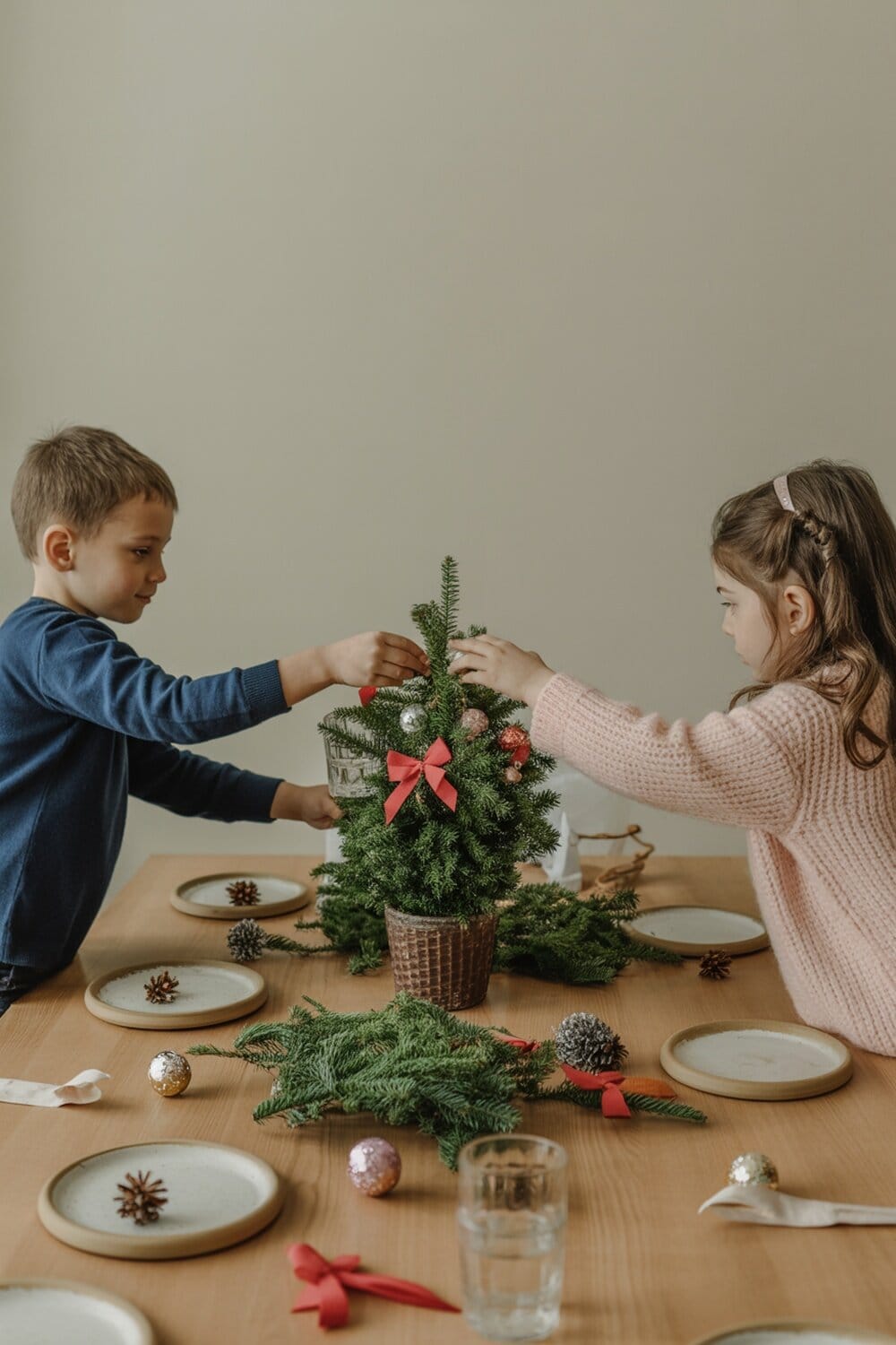 Kids decorating a small Christmas tree centerpiece with ornaments and ribbons.