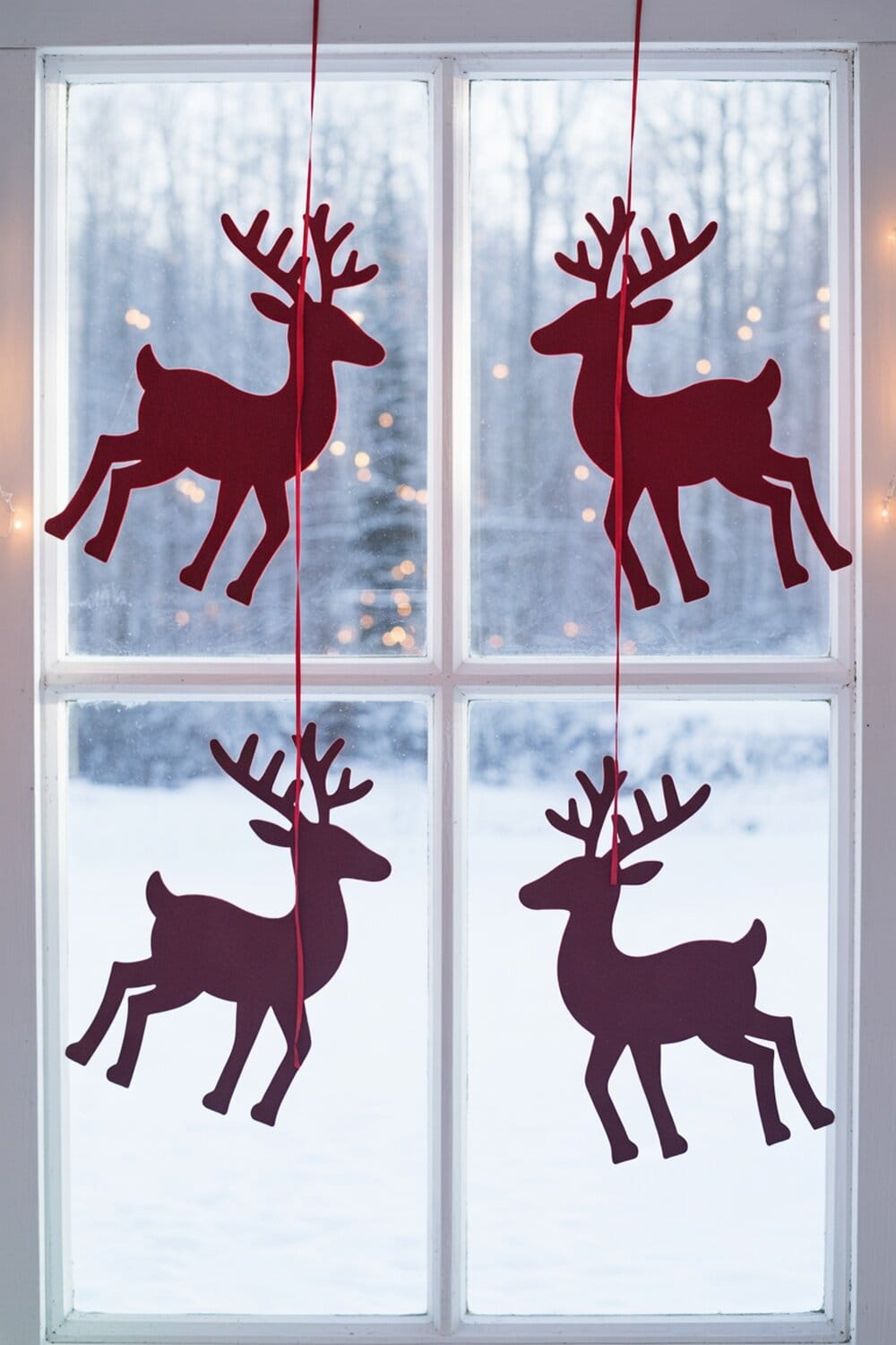 Felt reindeer silhouettes hanging in a window with a snowy background