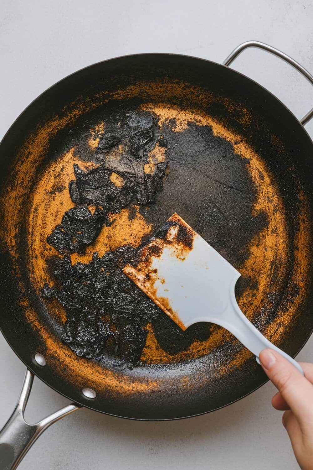 A hand using a plastic scraper on a burnt pan.