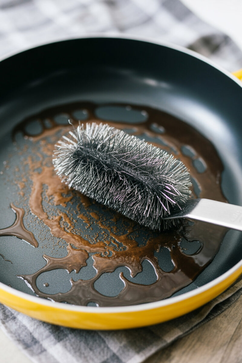 A pan with brown residue and a metal scrub brush.