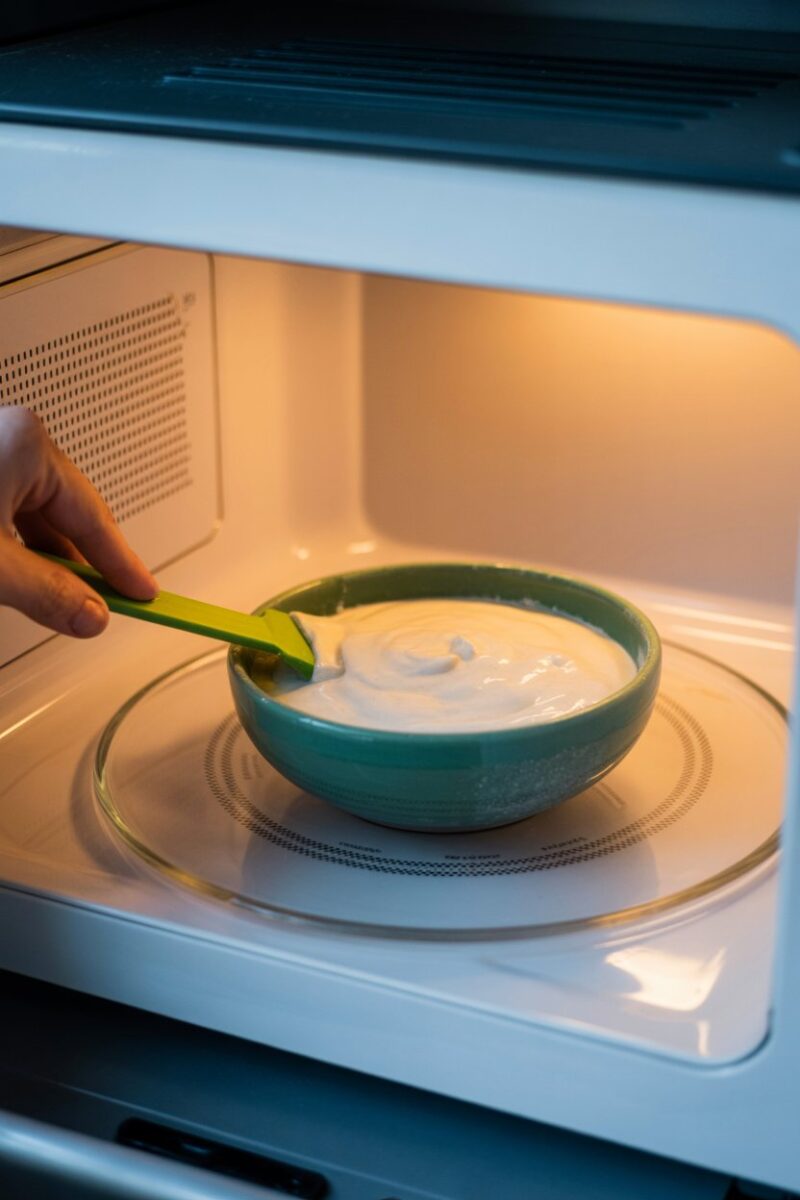 A bowl of cornstarch and water paste inside a microwave with a spatula.