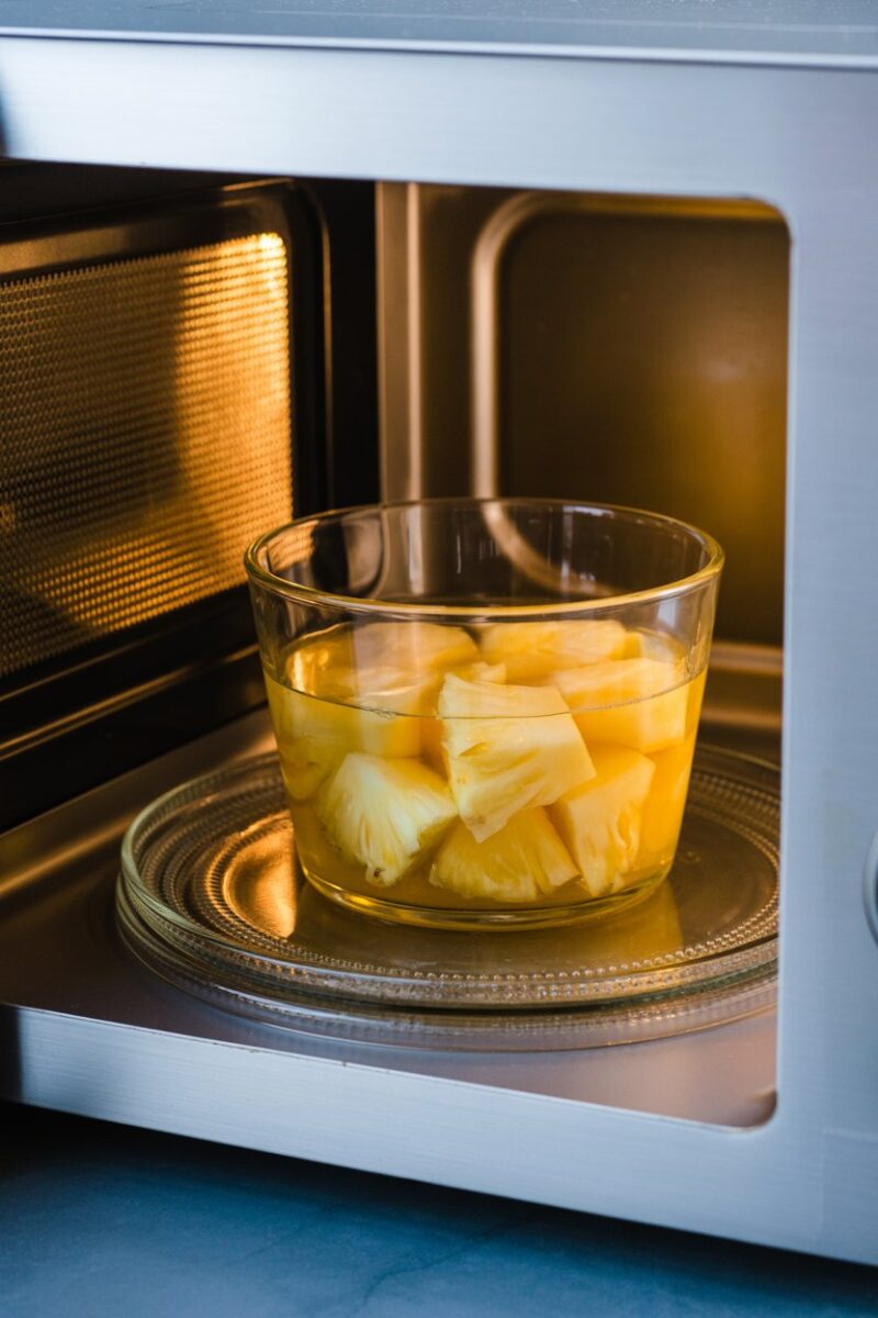 A bowl of pineapple juice and chunks inside a microwave.