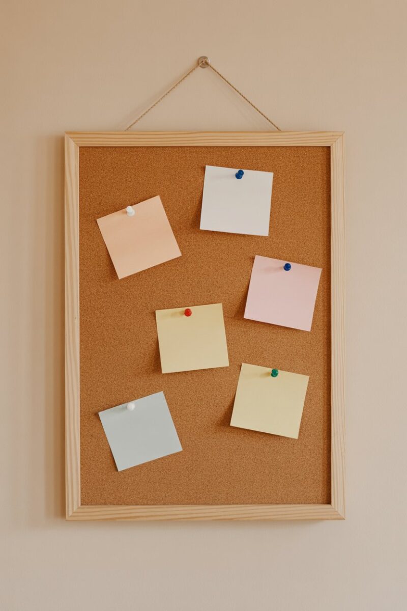 A cork board mounted on a wall with notes and reminders pinned on it.