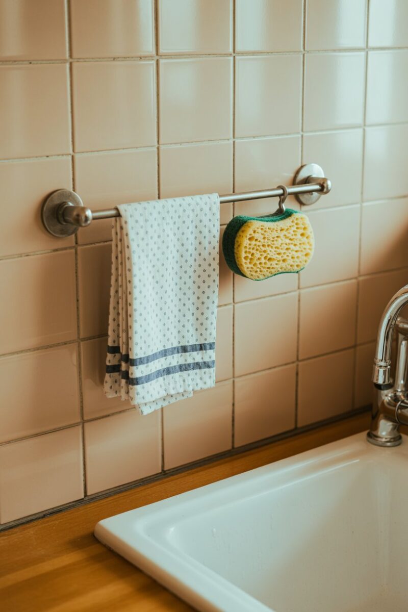 A kitchen sink area with a tension rod holding dish towels and a sponge.
