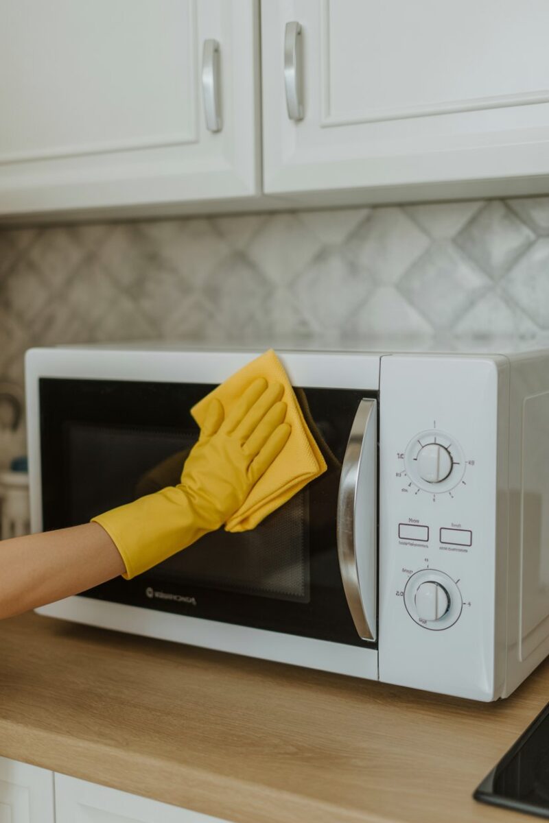 A person cleaning a microwave with a yellow cloth.